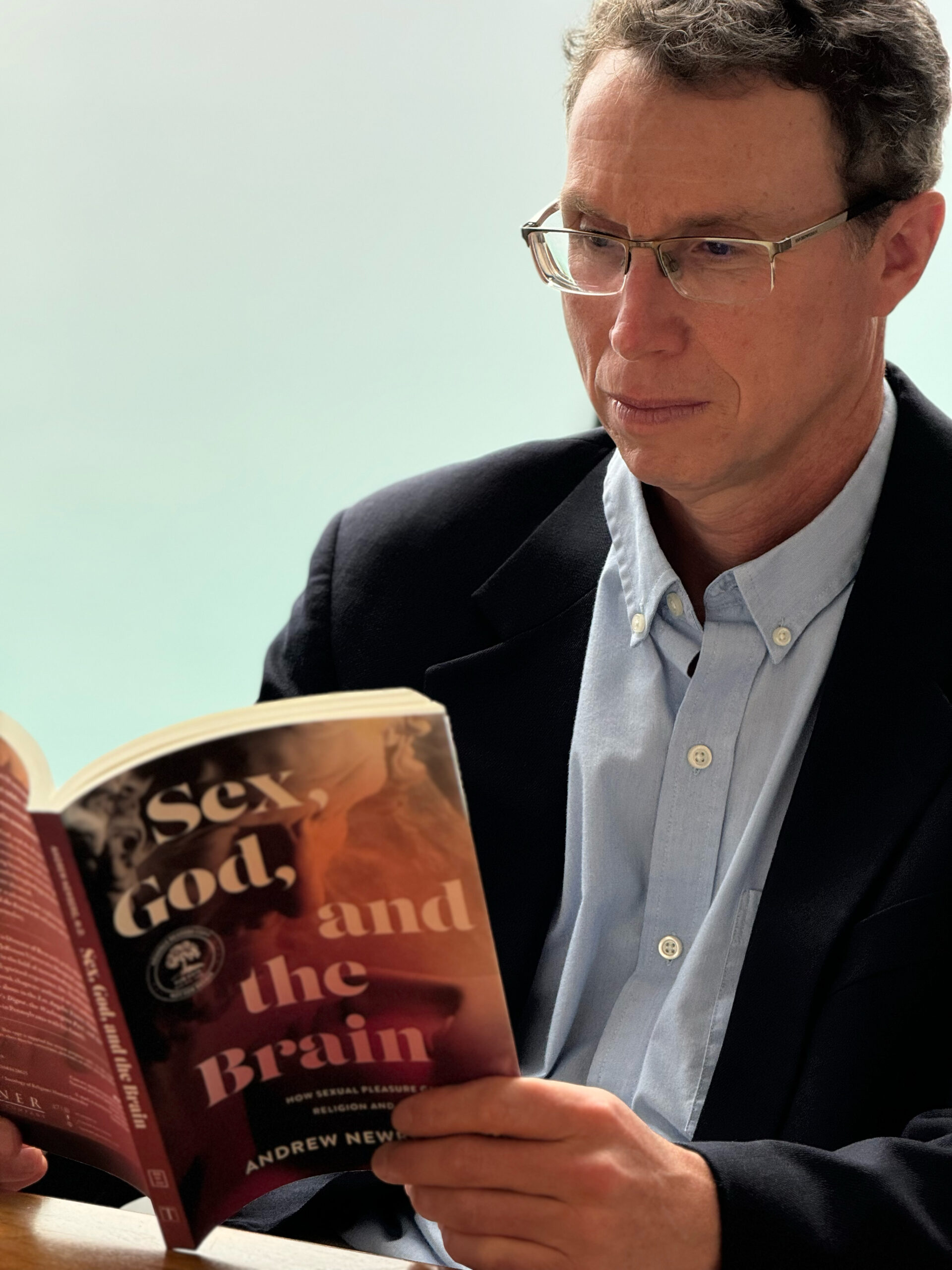 Doctor reading a book on spirituality and sexuality, titled 'Sex, God, and the Brain'.